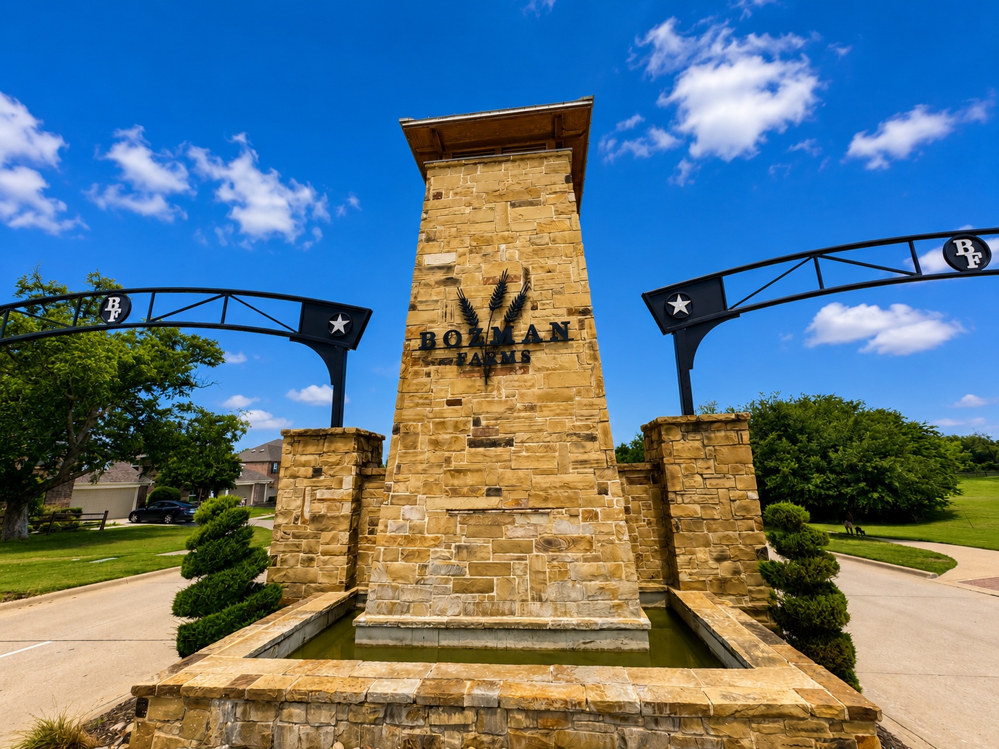 Bozman Farms entrance: tall stone tower with the sign, flanked by curved metal arches and a water feature at the base under a blue sky.