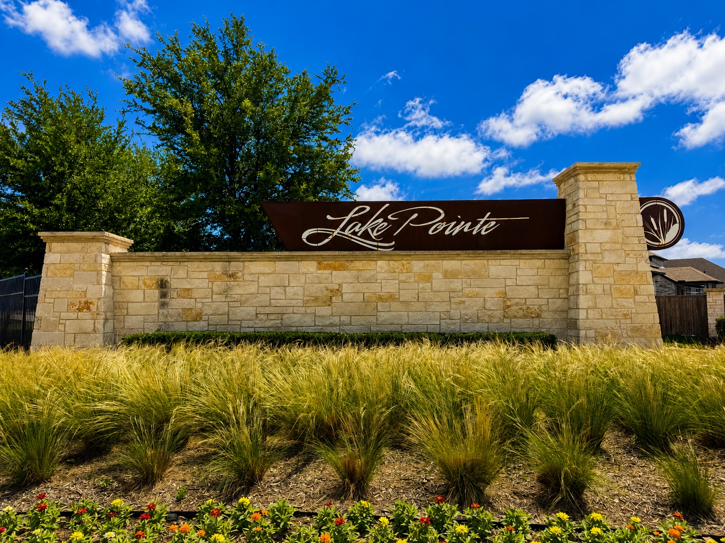 Stone entrance sign that reads Lake Pointe, set in a cream stone wall with blue sky and trees behind.