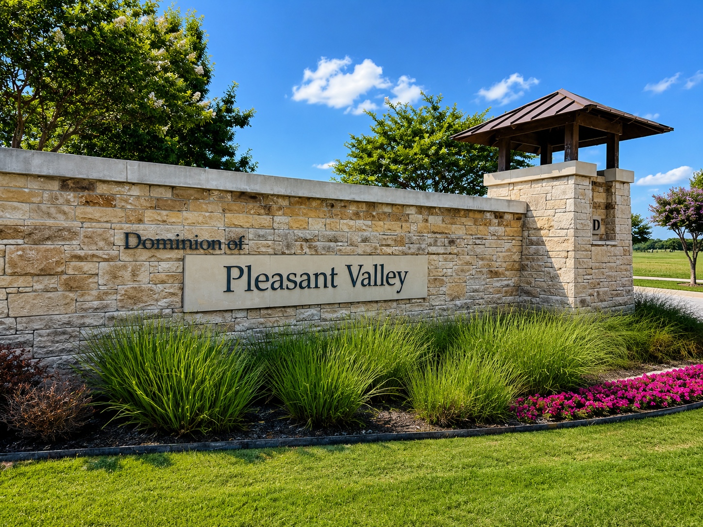 Stone entrance sign reading 'Dominion of Pleasant Valley' with green shrubs and a blue sky backdrop