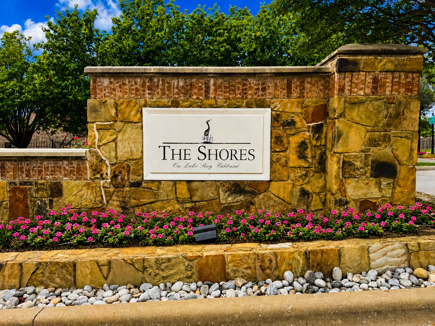 Stone entrance sign reading 'Dominion of Pleasant Valley' with green shrubs and a blue sky backdrop